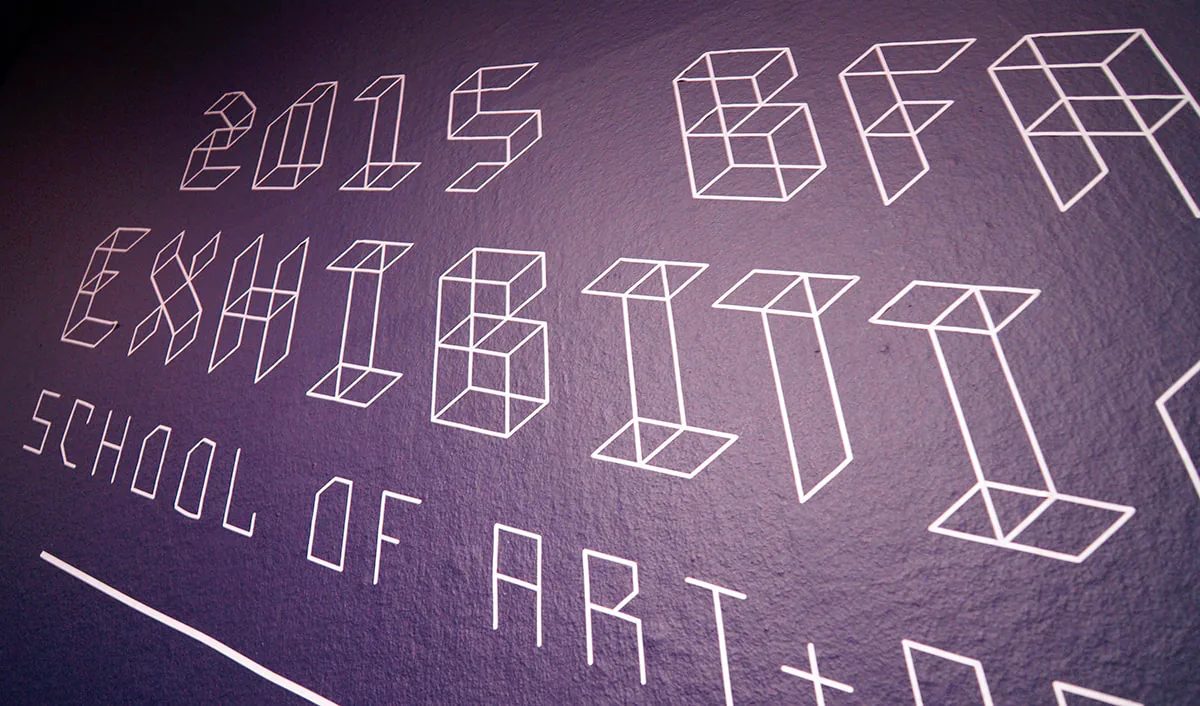 Close-up on printed lettering reading ‘2015 BFA Exhibition, School of Art+Design’ built from isometric cube-form letters