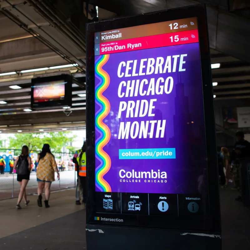Digital ad on an “L” station kiosk reading ‘Celebrate Chicago Pride Month’ beside a rainbow wave, with colum.edu/pride