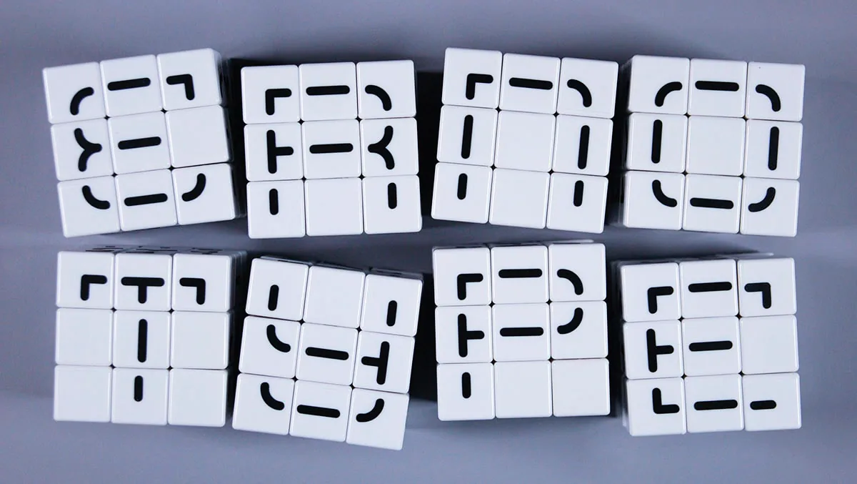 Overhead view of eight solved Erno Type cube faces, each spelling out a different letterform from the modular stroke system