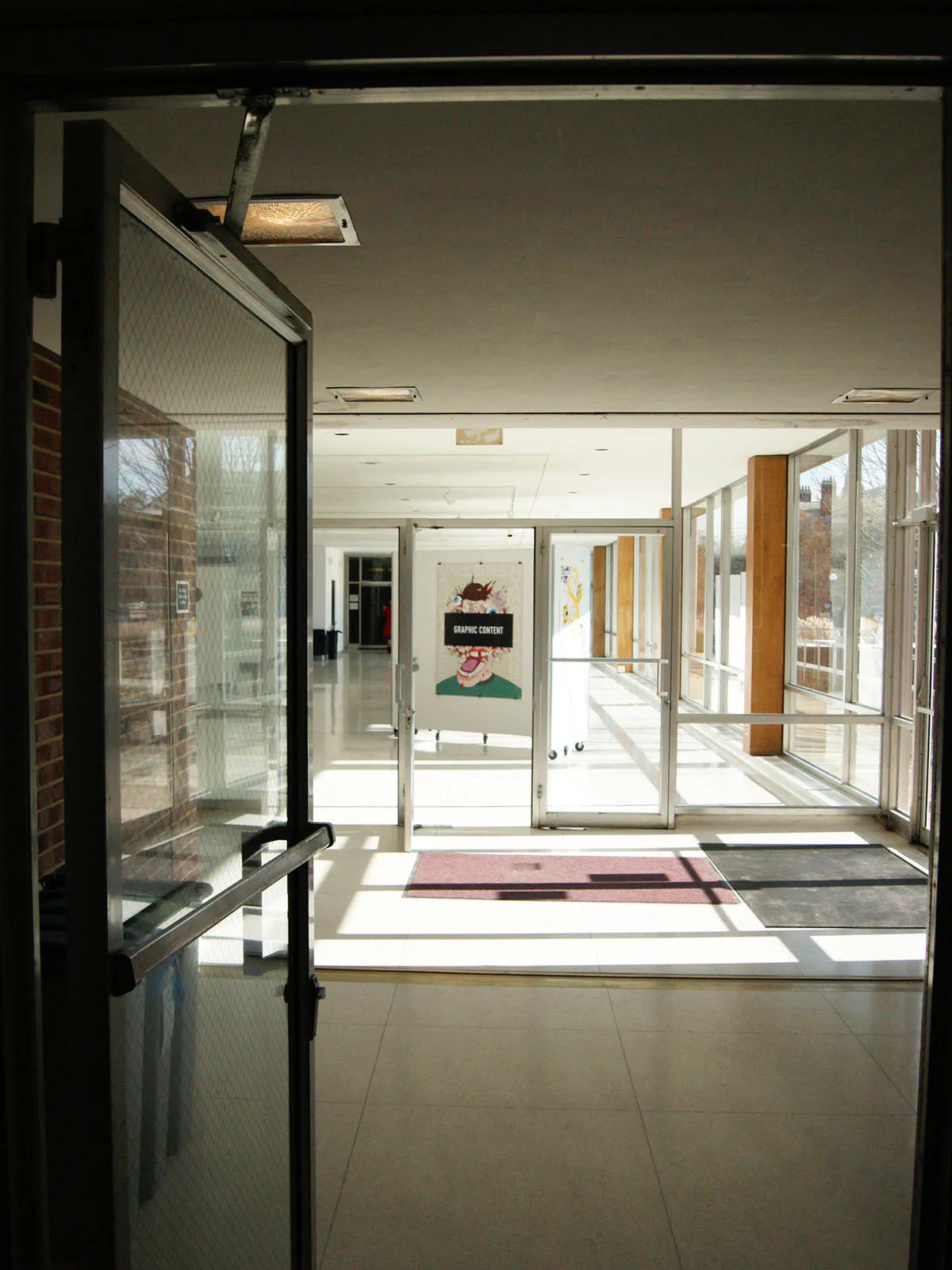 The ‘Graphic Content’ poster hung inside a glass-walled campus hallway, seen through an open doorway