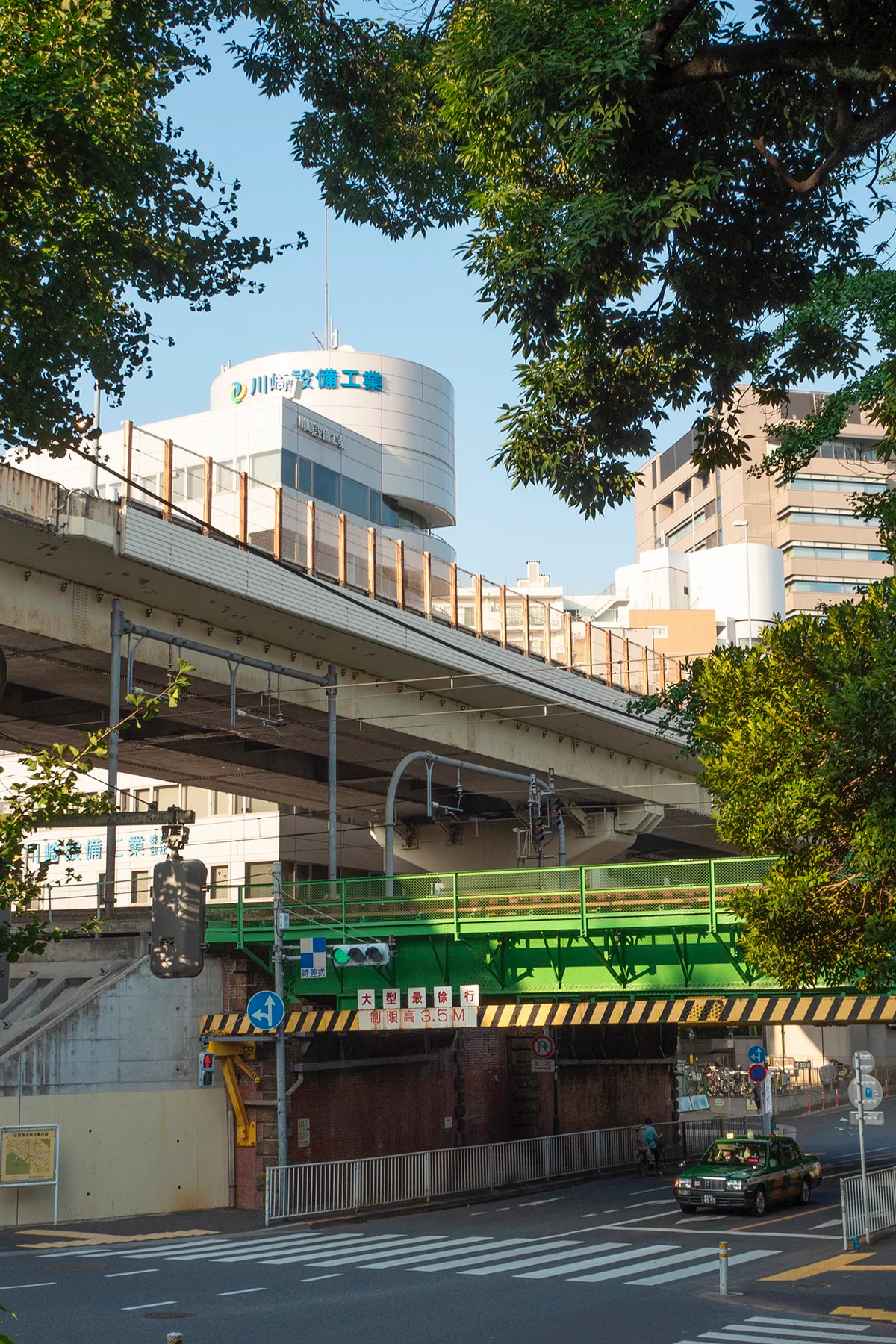 Green and gray elevated highway overpasses crisscross beneath a rounded corporate building, framed by tree branches