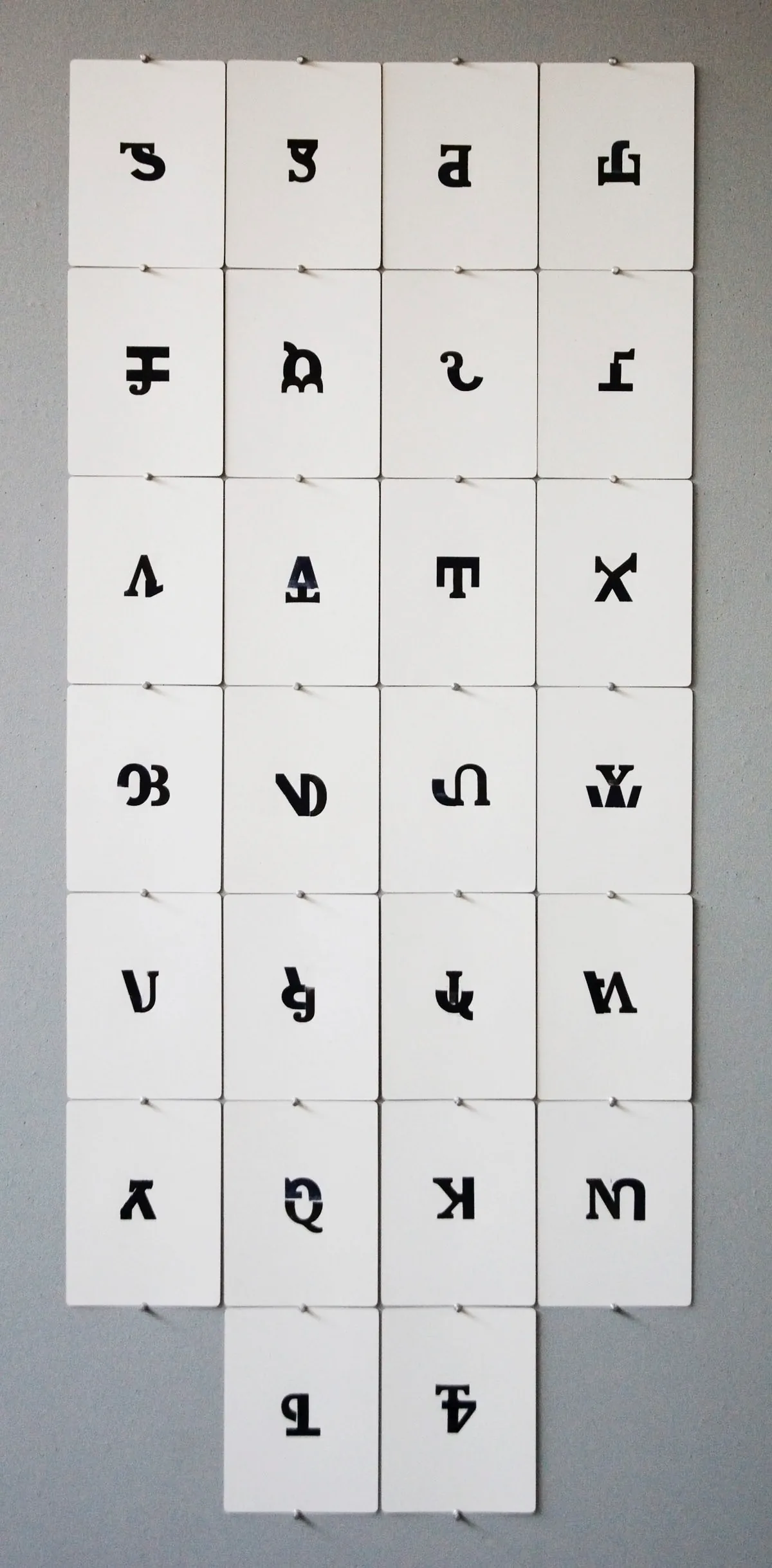 Grid of individually inked blackletter-style wood type characters pinned in rows on a gallery wall