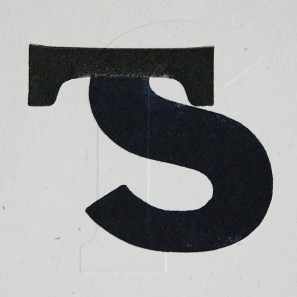 Close-up of a wood type letter S printed in letterpress, selectively inked in navy and black