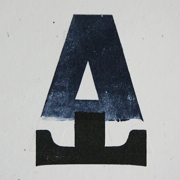 Close-up of a wood type letter A printed in letterpress, fading from navy at the top to solid black at the base