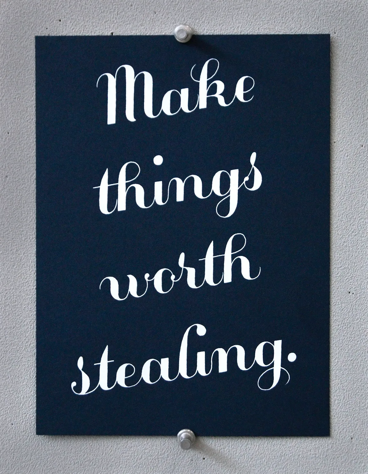 Screen print in flowing white script reading ‘Make things worth stealing.’ on dark navy paper