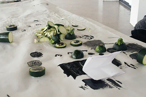 Worktable scattered with zucchini scraps and ink-stamped letterform proofs