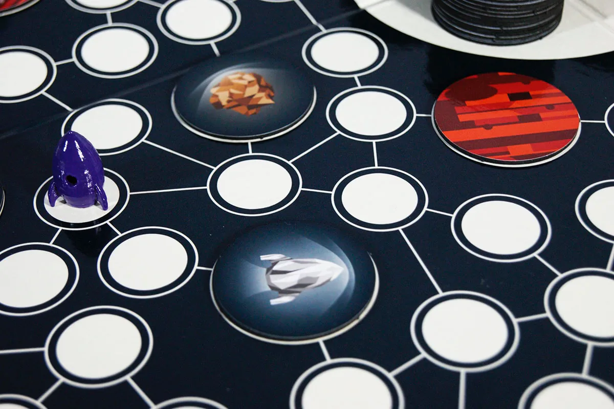Close-up of the Terra Nova board with a purple rocket piece beside glowing planet tiles