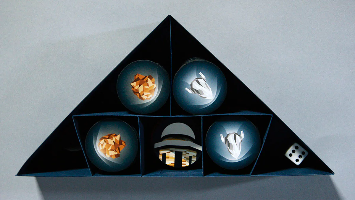 Inside the triangular Terra Nova box, showing stacked planet tiles and a die tucked into laser-cut chipboard slots